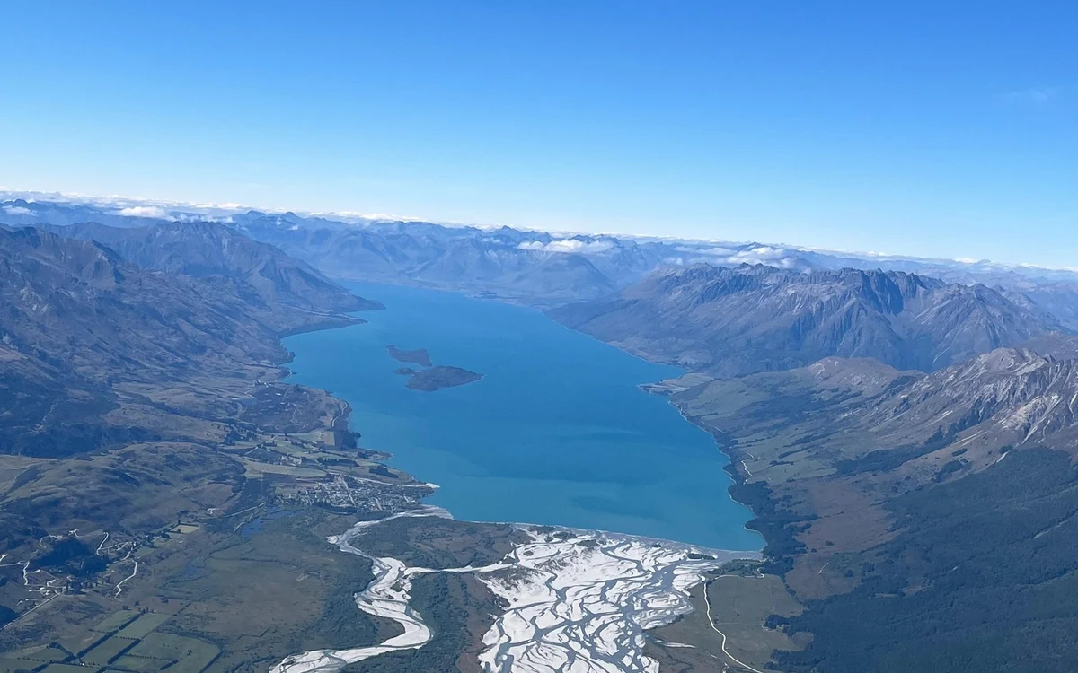 Braided river channels spreading across a wide valley floor seen from a helicopter window