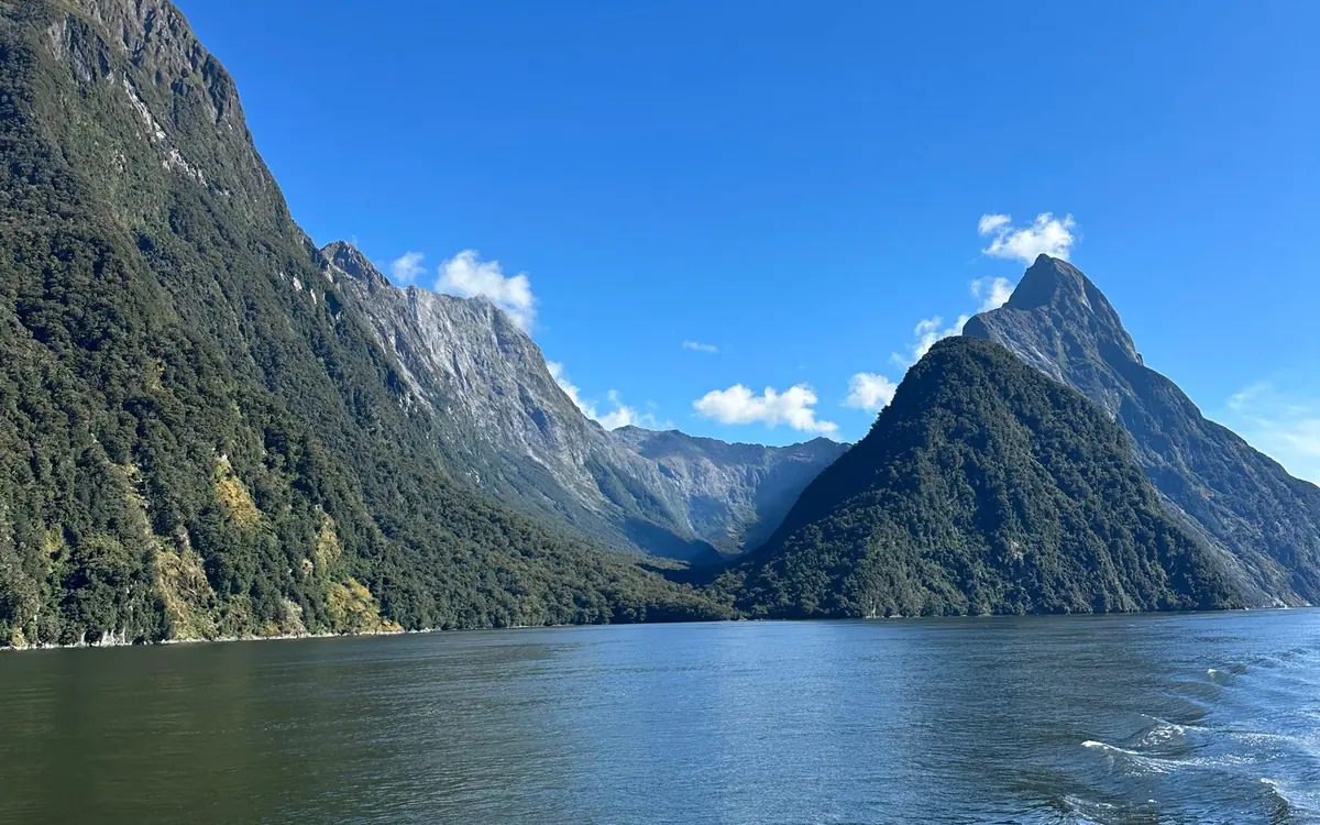 A helicopter above a deep fiord with waterfalls falling from forested walls into dark water