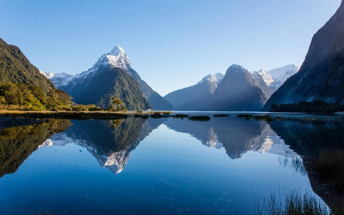 A steep pyramid peak rising straight out of dark fiord water seen from the air
