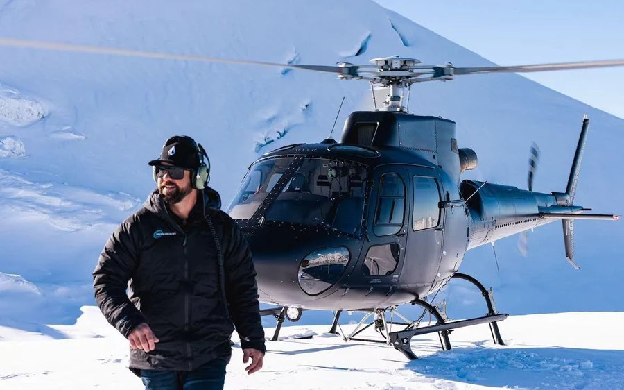 Deep blue glacier ice under a thin cover of snow with a helicopter behind