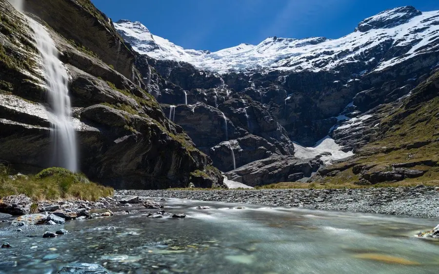 A hanging glacier above a green valley with waterfalls falling down the rock face