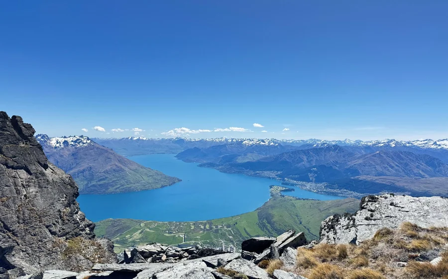 Snow-streaked peaks and a deep blue lake seen from a helicopter window