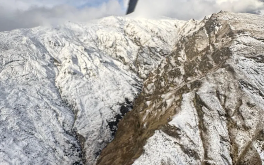 A helicopter on a snowfield with passengers standing on the snow beside it
