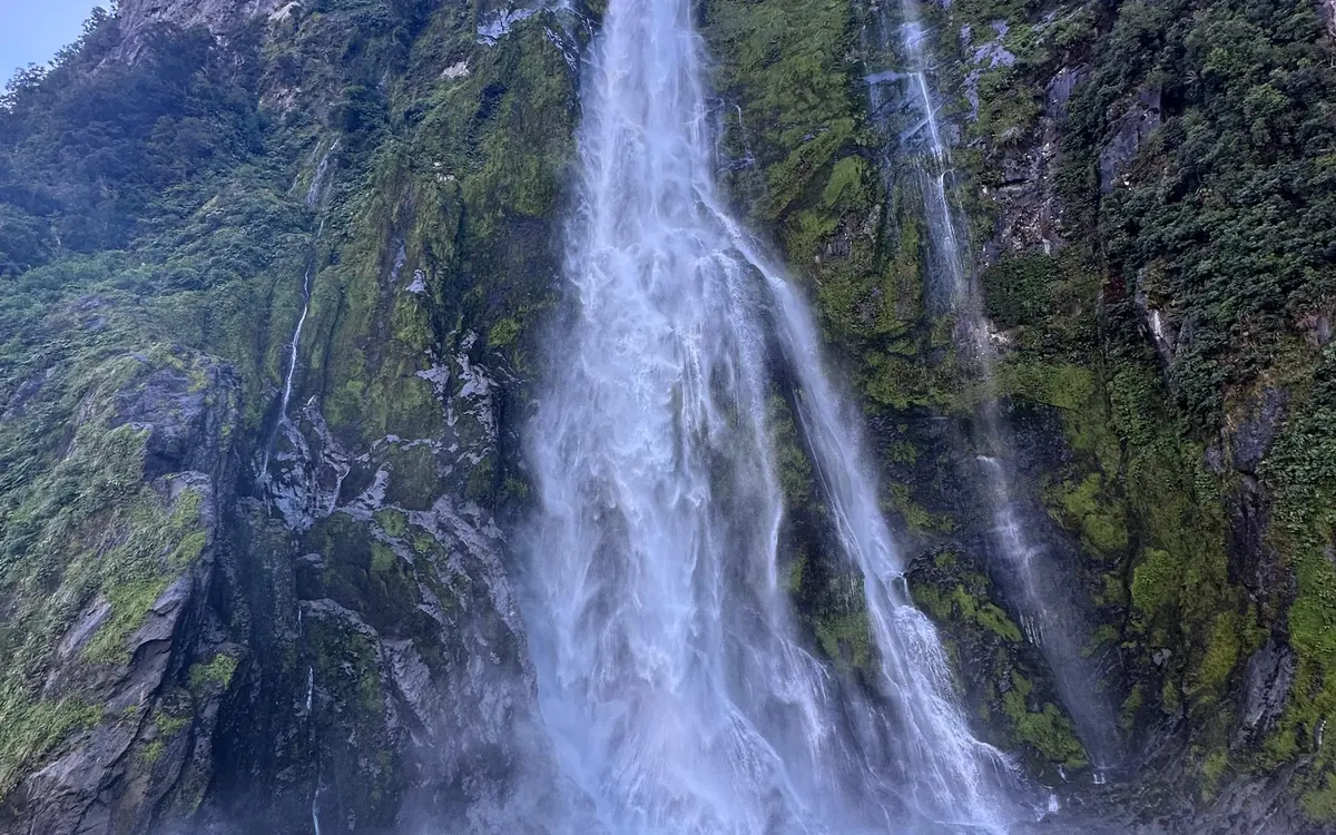 A waterfall falling down a rock wall into the water of a fiord